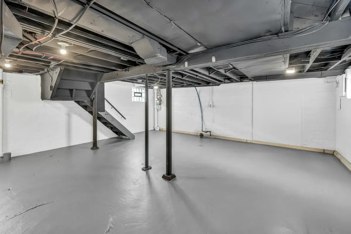 An unfinished basement with exposed joists, steel posts and stairs