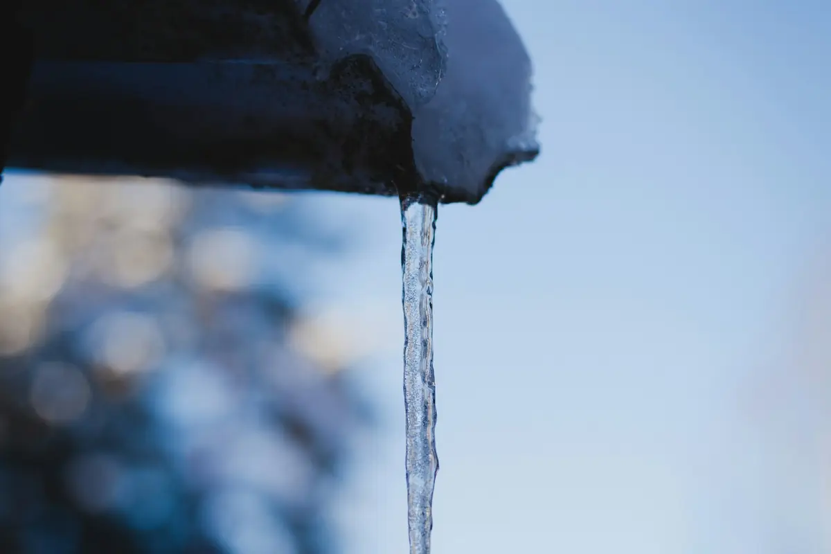 A single icicle hanging from a snowy roof edge